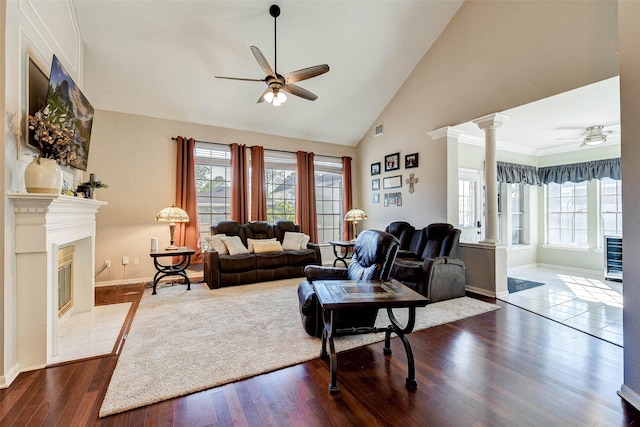 living room featuring high vaulted ceiling, ceiling fan, ornate columns, a fireplace, and wood-type flooring