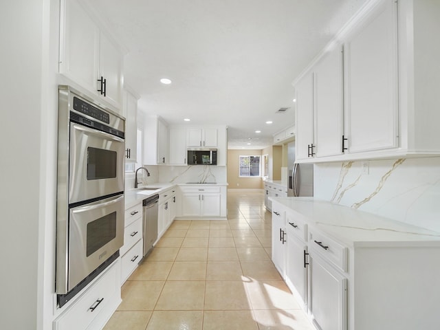 kitchen with appliances with stainless steel finishes, tasteful backsplash, sink, light tile patterned floors, and white cabinets