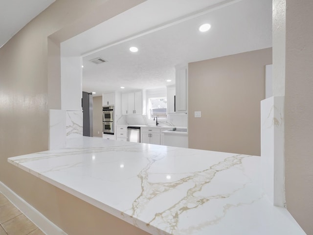 kitchen with white cabinetry, sink, light stone counters, kitchen peninsula, and appliances with stainless steel finishes