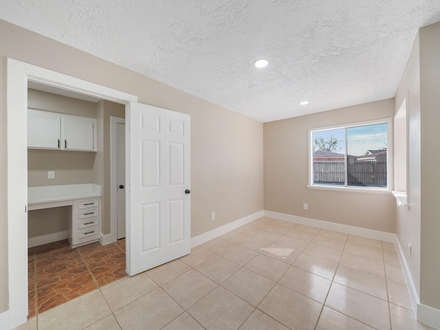 unfurnished bedroom featuring built in desk, a textured ceiling, and light tile patterned floors