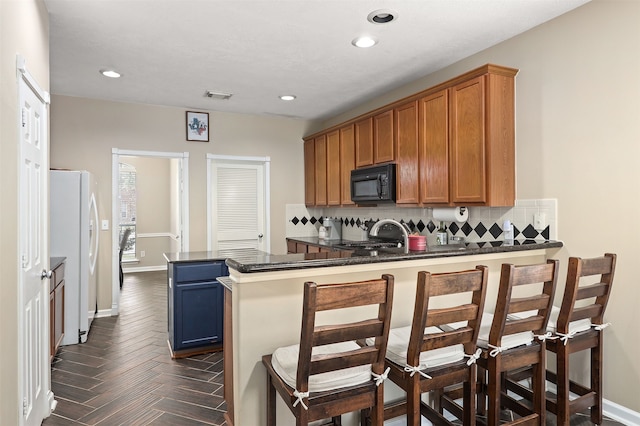 kitchen featuring kitchen peninsula, a kitchen breakfast bar, white fridge, and tasteful backsplash