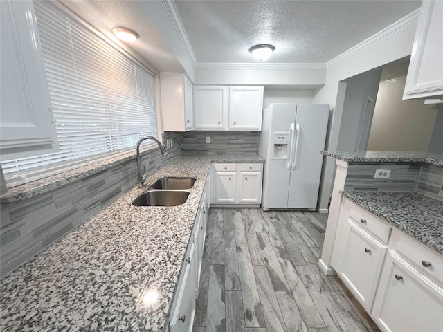 kitchen featuring white refrigerator with ice dispenser, backsplash, white cabinets, sink, and stone countertops