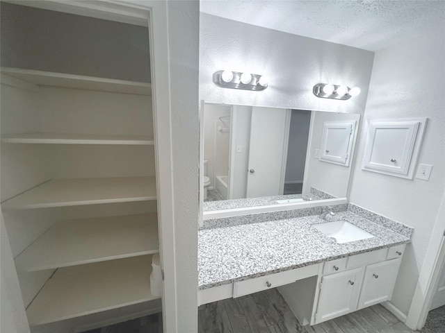 bathroom with vanity, hardwood / wood-style flooring, ceiling fan, toilet, and a textured ceiling