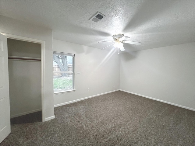 unfurnished bedroom with a textured ceiling, a closet, dark carpet, and ceiling fan