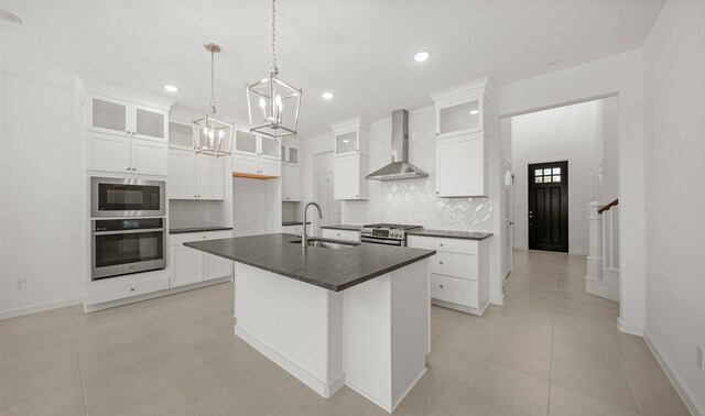 kitchen featuring sink, wall chimney exhaust hood, decorative backsplash, a center island with sink, and appliances with stainless steel finishes