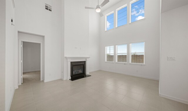 unfurnished living room with ceiling fan, light tile patterned floors, a healthy amount of sunlight, and a high ceiling