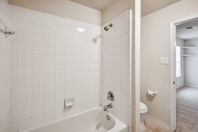 bathroom with a textured ceiling, toilet, and tiled shower / bath