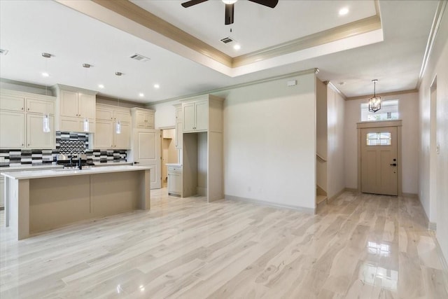 kitchen featuring light wood-type flooring, sink, a center island with sink, cream cabinetry, and hanging light fixtures