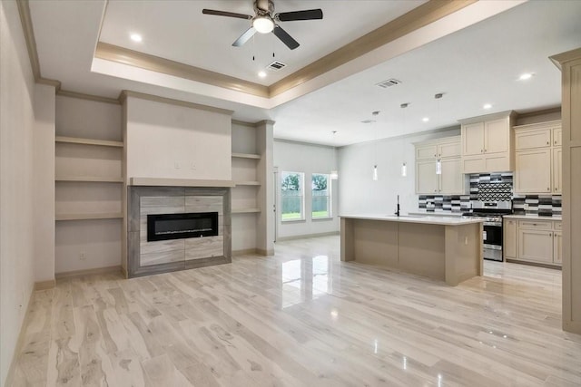 kitchen with cream cabinets, an island with sink, a tiled fireplace, and stainless steel range oven