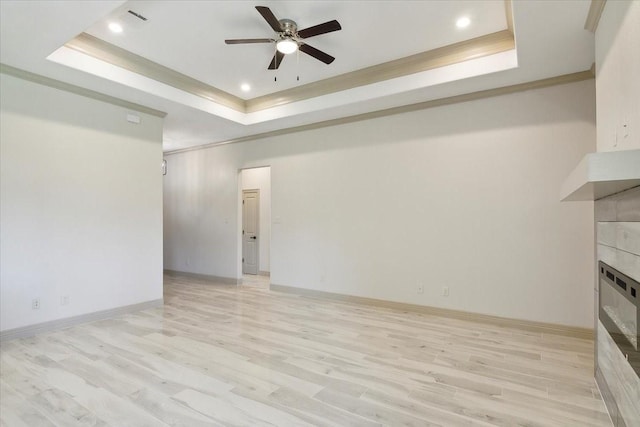 unfurnished living room featuring a tray ceiling, ceiling fan, a fireplace, and light hardwood / wood-style floors