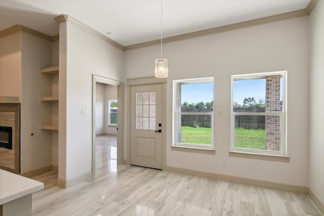 interior space with a fireplace, ornamental molding, light wood-type flooring, and a healthy amount of sunlight