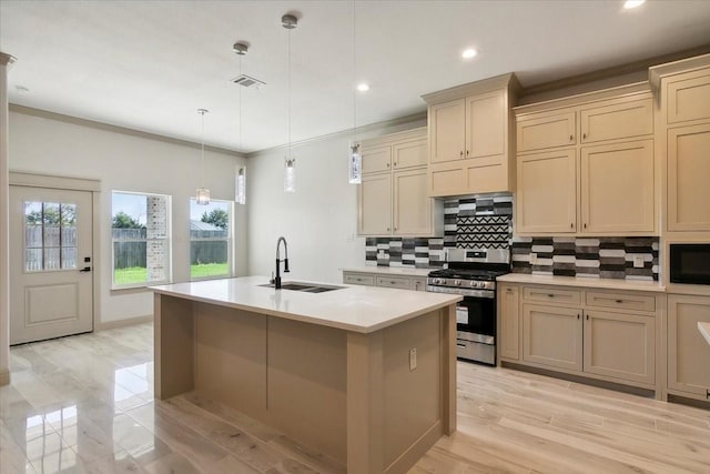 kitchen featuring stainless steel gas range oven, a kitchen island with sink, sink, cream cabinetry, and hanging light fixtures