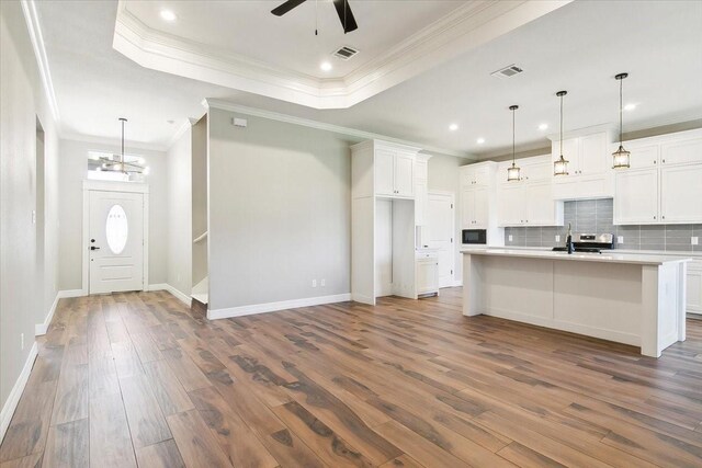 kitchen with ornamental molding, a kitchen island with sink, dark wood-type flooring, pendant lighting, and white cabinets