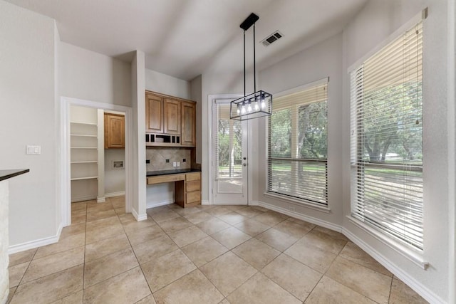 unfurnished dining area featuring vaulted ceiling, light tile patterned flooring, and built in desk