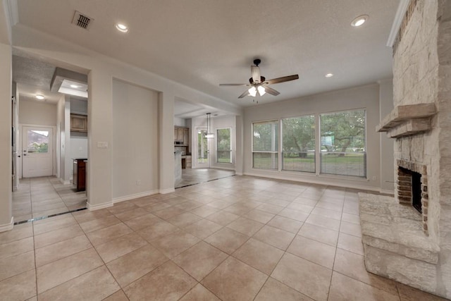 unfurnished living room featuring ceiling fan, light tile patterned flooring, a stone fireplace, and a healthy amount of sunlight