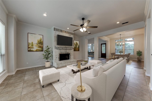 living room with light tile patterned floors, ornamental molding, a fireplace, and ceiling fan with notable chandelier