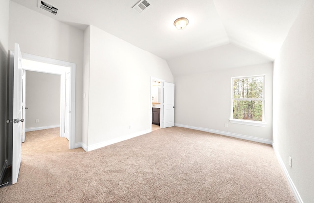 unfurnished bedroom featuring light colored carpet, lofted ceiling, and ensuite bathroom