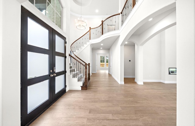 foyer featuring a high ceiling, french doors, light wood-type flooring, ornamental molding, and a chandelier