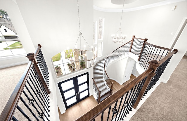 stairway featuring french doors, crown molding, a chandelier, a high ceiling, and carpet floors