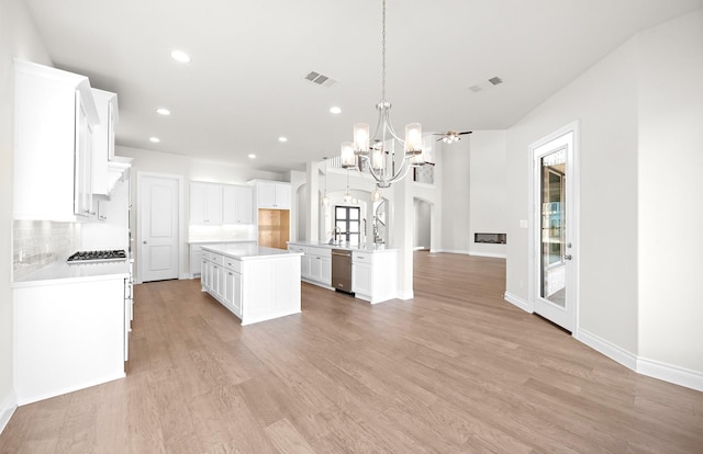 kitchen with light wood-type flooring, stainless steel dishwasher, a fireplace, white cabinets, and a kitchen island