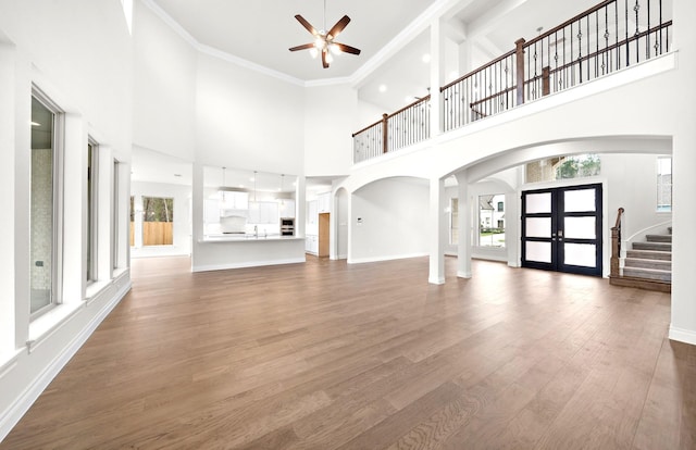 unfurnished living room featuring hardwood / wood-style floors, high vaulted ceiling, french doors, crown molding, and ceiling fan