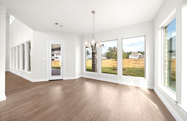 unfurnished dining area with an inviting chandelier, a wealth of natural light, and dark wood-type flooring