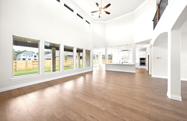 unfurnished living room with hardwood / wood-style floors, ceiling fan, ornamental molding, and a high ceiling