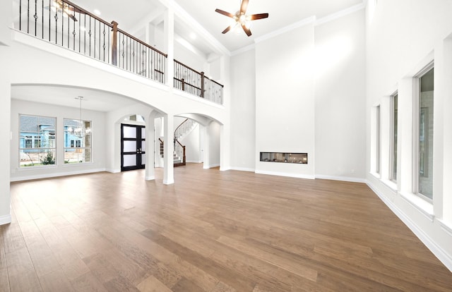 unfurnished living room with hardwood / wood-style floors, ceiling fan, crown molding, and a high ceiling