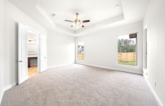 unfurnished bedroom featuring ceiling fan, light colored carpet, and a tray ceiling