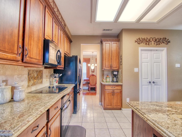 kitchen featuring light stone counters, an inviting chandelier, tasteful backsplash, and black appliances