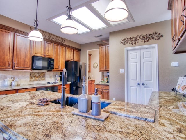 kitchen with black appliances, pendant lighting, light stone counters, and backsplash