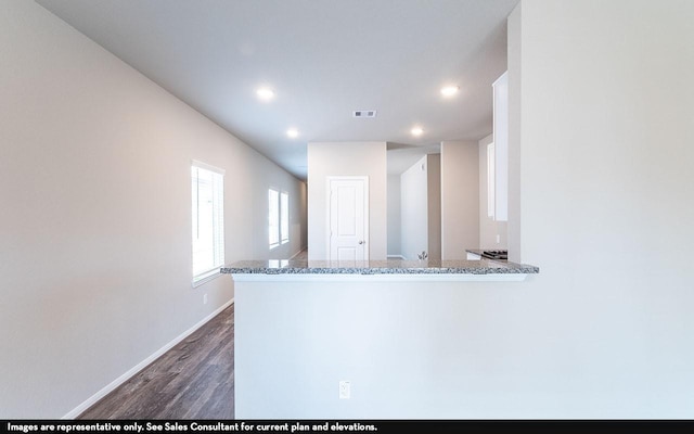 kitchen with dark hardwood / wood-style flooring, kitchen peninsula, and light stone counters