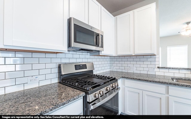 kitchen with decorative backsplash, white cabinetry, appliances with stainless steel finishes, and dark stone counters