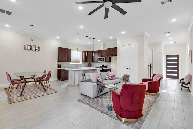 living room featuring light wood-type flooring, ceiling fan with notable chandelier, crown molding, and sink