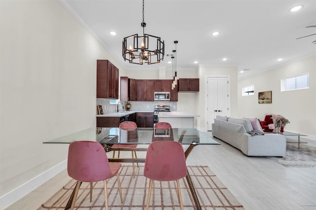 dining space with crown molding, sink, an inviting chandelier, and light wood-type flooring