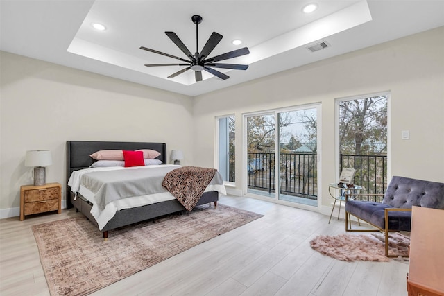 bedroom with access to exterior, a tray ceiling, light hardwood / wood-style flooring, and ceiling fan