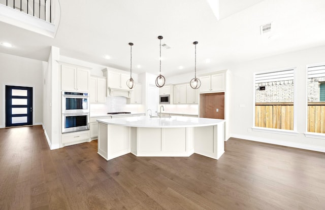 kitchen with dark wood-type flooring, white cabinetry, a center island with sink, and stainless steel appliances