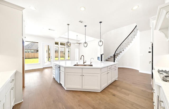 kitchen with sink, decorative light fixtures, a center island with sink, light hardwood / wood-style flooring, and white cabinets