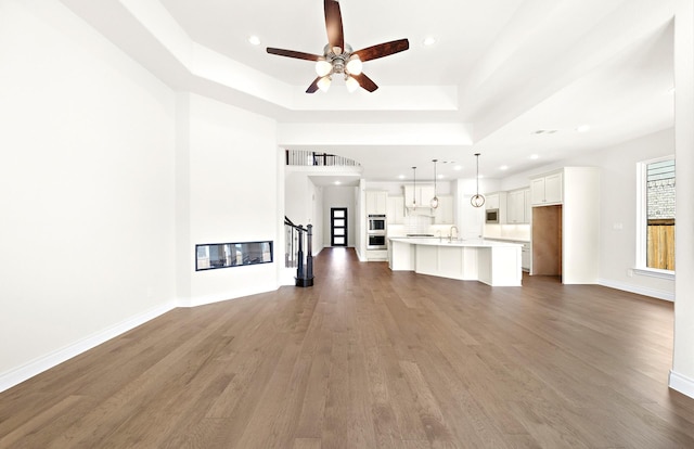 unfurnished living room featuring dark hardwood / wood-style floors, ceiling fan, sink, and a tray ceiling