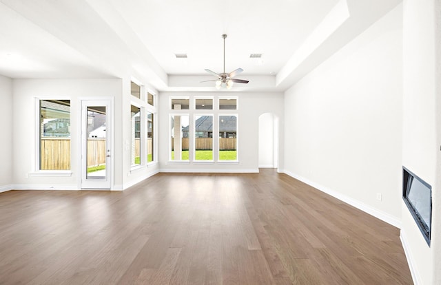 unfurnished living room featuring dark hardwood / wood-style floors, ceiling fan, and a tray ceiling