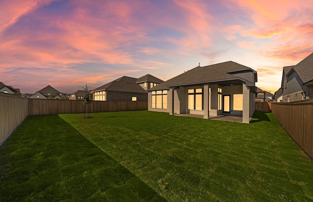 back house at dusk featuring a patio area and a yard