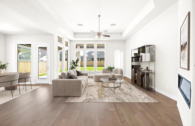 living room featuring ceiling fan, dark wood-type flooring, and a tray ceiling