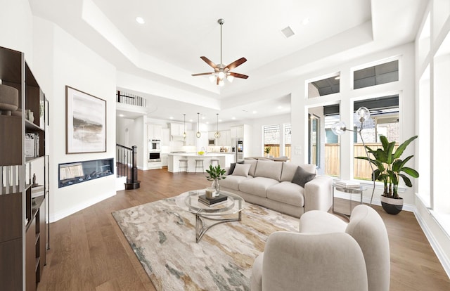 living room featuring hardwood / wood-style floors, a tray ceiling, and ceiling fan