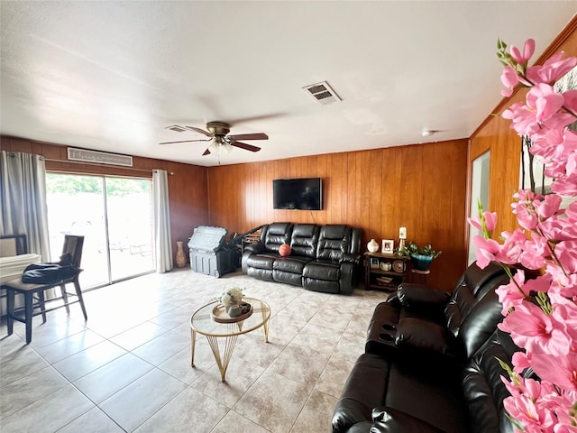 living room with light tile patterned floors, ceiling fan, and wood walls