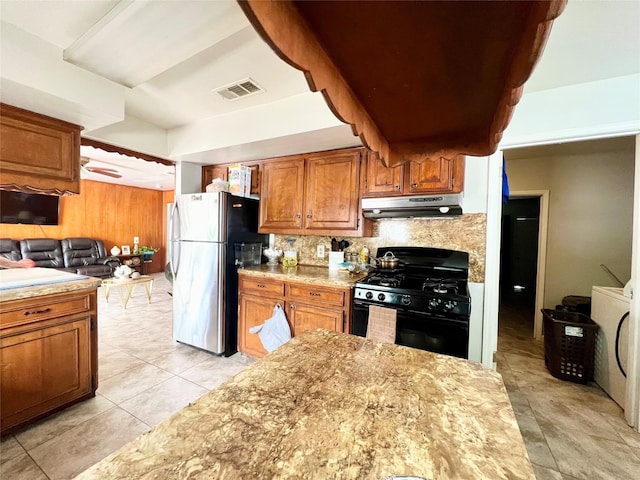 kitchen featuring light tile patterned floors, gas stove, stainless steel refrigerator, and backsplash