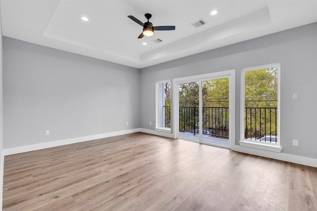 empty room with a tray ceiling, ceiling fan, and light hardwood / wood-style floors