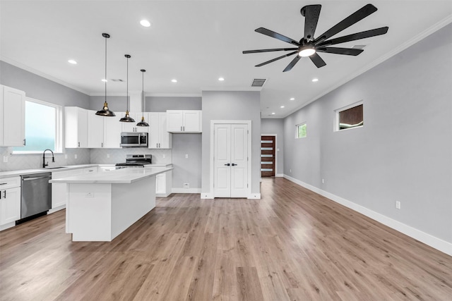 kitchen with a center island, appliances with stainless steel finishes, pendant lighting, white cabinets, and light wood-type flooring