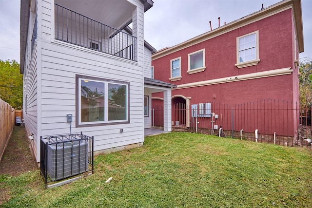 rear view of property with a lawn, central AC unit, and a balcony