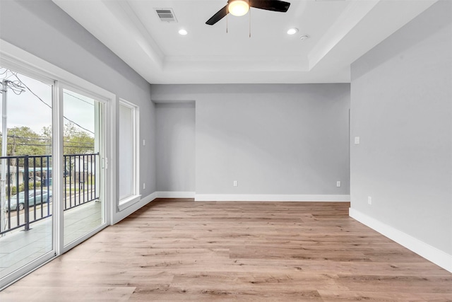 empty room with a tray ceiling, ceiling fan, and light wood-type flooring