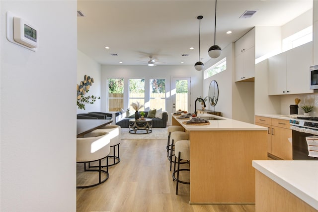 kitchen featuring pendant lighting, a kitchen island with sink, a kitchen breakfast bar, sink, and white cabinetry